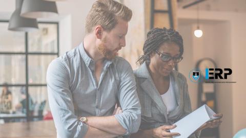 Two persons leaning against a desk looking at a paper document